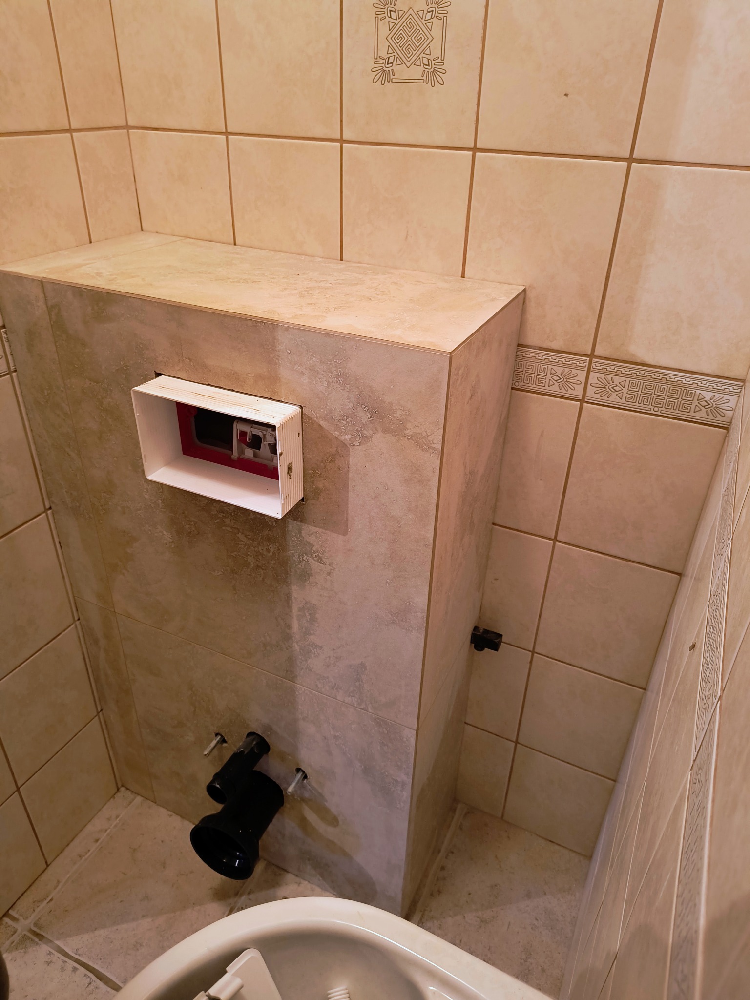 Wnęka z zabudową podtynkową WC w trakcie montażu, widoczne elementy instalacji i stelaż, beżowe płytki ceramiczne na ścianach.