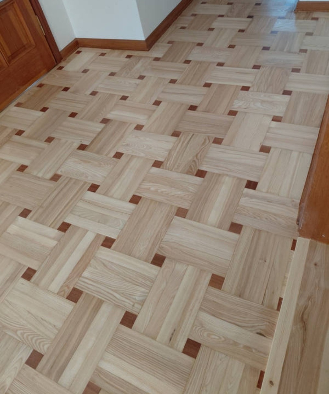 Parkiet w jodełkę francuską z jasnego drewna i ciemnymi akcentami, ułożony w Leoncin. Wykończenie podłogi z listwami przypodłogowymi.