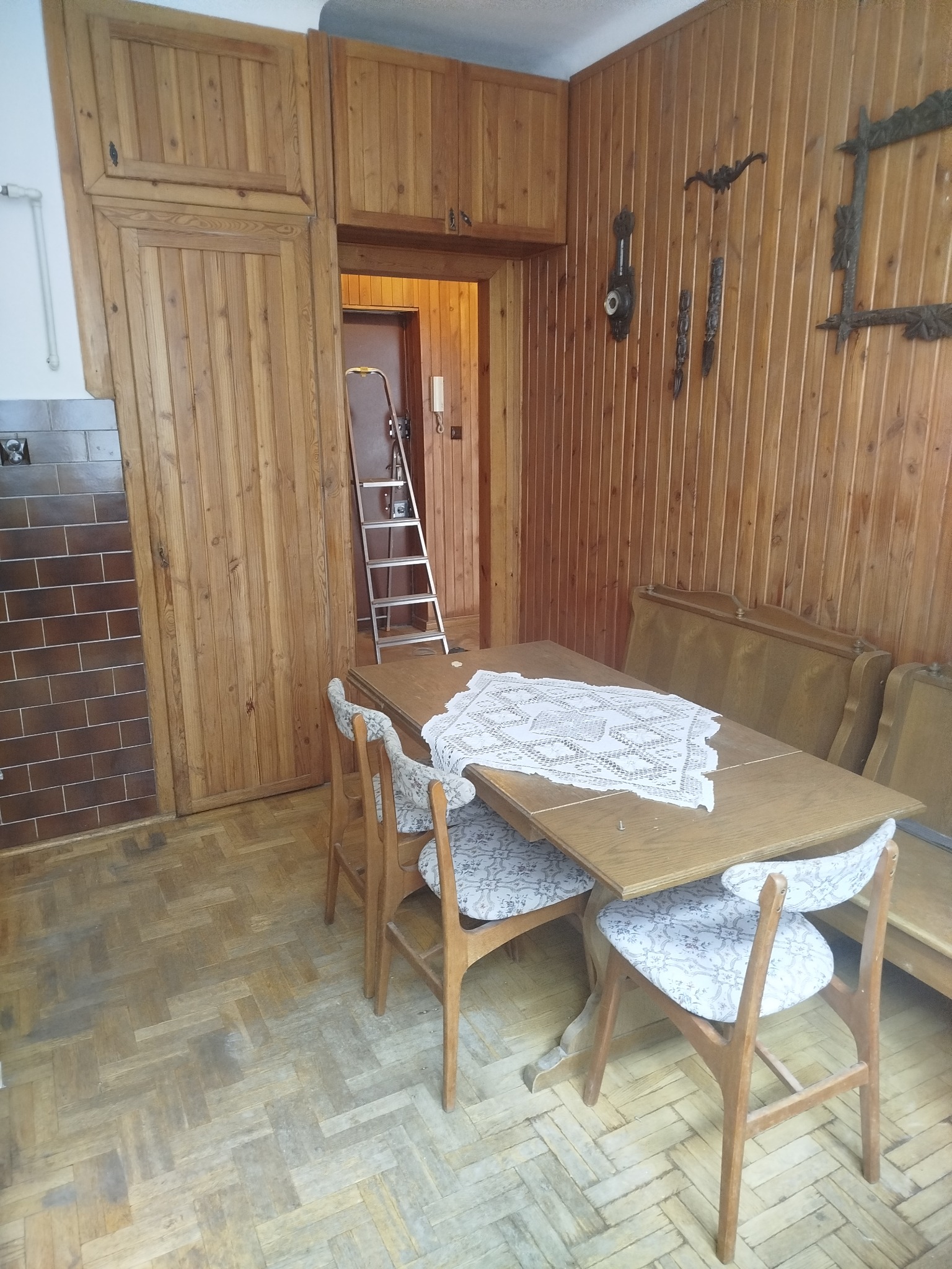 Drewniane wnętrze z parkietem ułożonym w jodełkę. Widoczne drewniane boazerie i meble. W tle drabina oparta o ścianę. Całość w ciepłej tonacji.