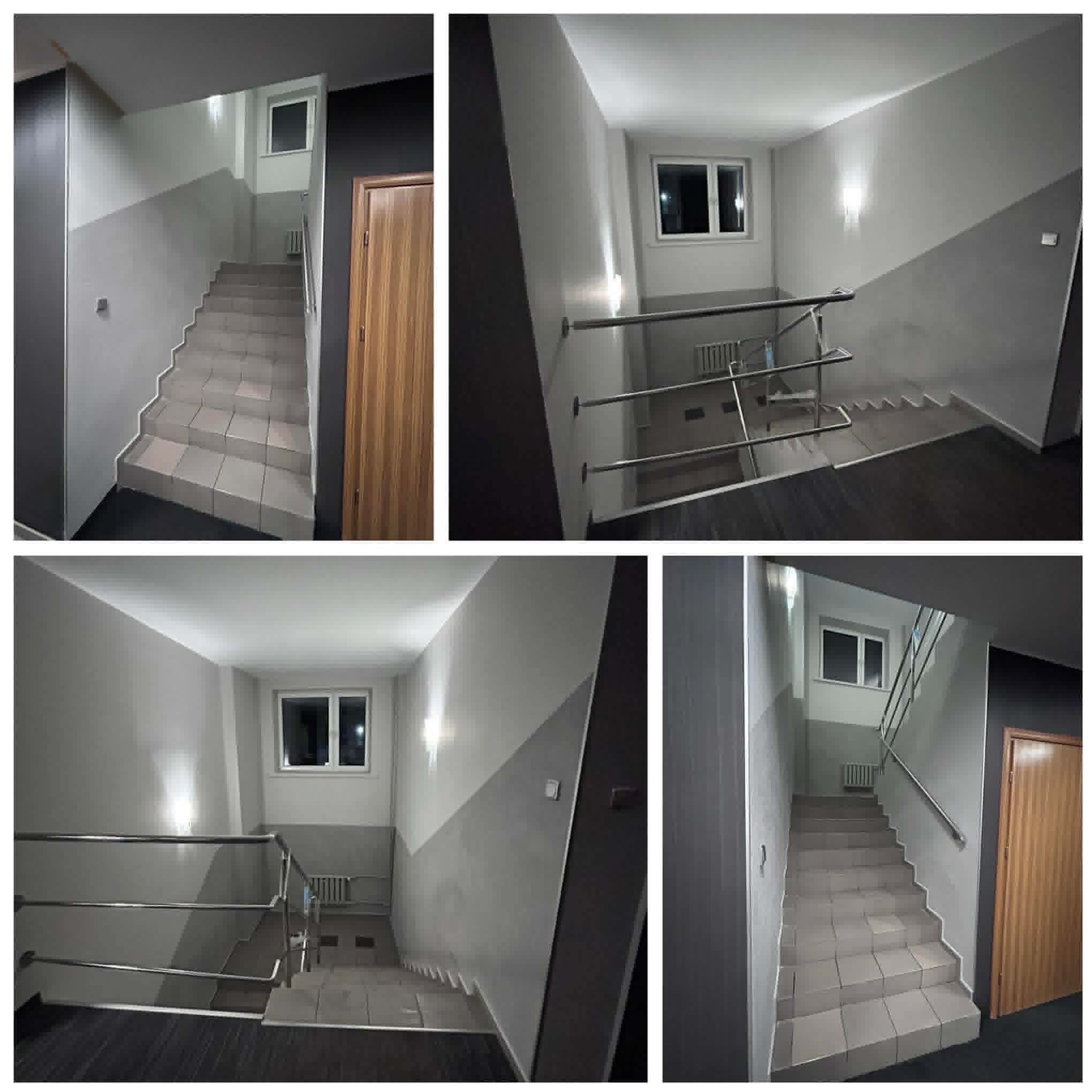 Klatka schodowa po remoncie: szare ściany z ukośnym podziałem kolorów, płytki na schodach, metalowe barierki, okno. Nowoczesne wykończenie.