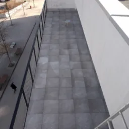 Wykończony taras na dachu budynku z szarych płyt. Widok z góry z elementami architektury miejskiej i pojedynczym stołkiem na środku.