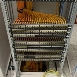 Panel krosowniczy z podłączonymi kablami sieciowymi, uporządkowane okablowanie w szafie serwerowej, widoczne porty RJ45 z numeracją.