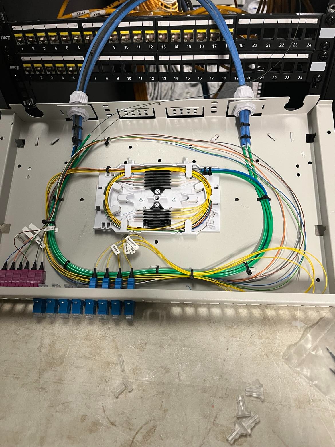 Panel krosowniczy światłowodowy z uporządkowanymi kablami w różnych kolorach, zakończonymi złączami; widoczne etykiety na kablach i porty patch panelu.
