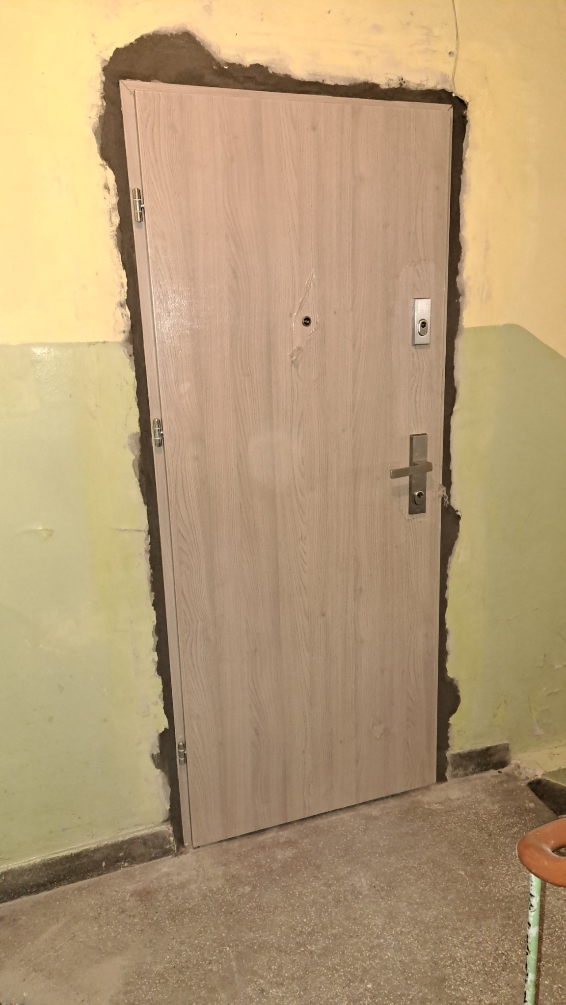 Montaż drzwi wejściowych z ościeżnicą w trakcie prac wykończeniowych, widoczne ślady po zaprawie na ścianie.