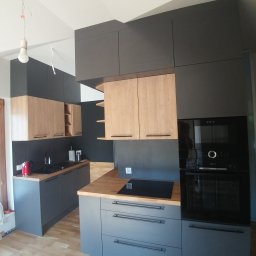 PROJEKT MG MARCIN GURTAT - Nowoczesna kuchnia z szarymi dolnymi szafkami i drewnopodobnymi górnymi, drewniany blat, płyta indukcyjna i wbudowany piekarnik, surowa żarówka zwisająca z sufitu.