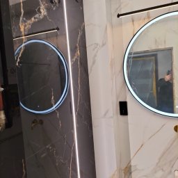 Usługi remontowo budowlane - Elegancka łazienka z marmurowymi płytkami, okrągłymi lustrami z podświetleniem LED i minimalistycznym oświetleniem. Czarno-biała kolorystyka.
