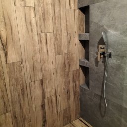 Usługi remontowo budowlane - Nowoczesna kabina prysznicowa z płytkami imitującymi drewno na ścianie i podłodze, oraz szarą płytką na ścianie z wnękami i deszczownicą.