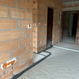 AZB Piotr Patoń - Instalacja elektryczna w trakcie wykonywania w Bytomiu: widoczne przewody ułożone na podłodze i puszki podtynkowe w ścianie z cegły kratówki.