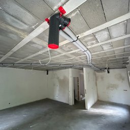 AZB Piotr Patoń - Szara instalacja wentylacyjna z czerwonymi elementami zamocowana do sufitu w surowym stanie w nowym pomieszczeniu.