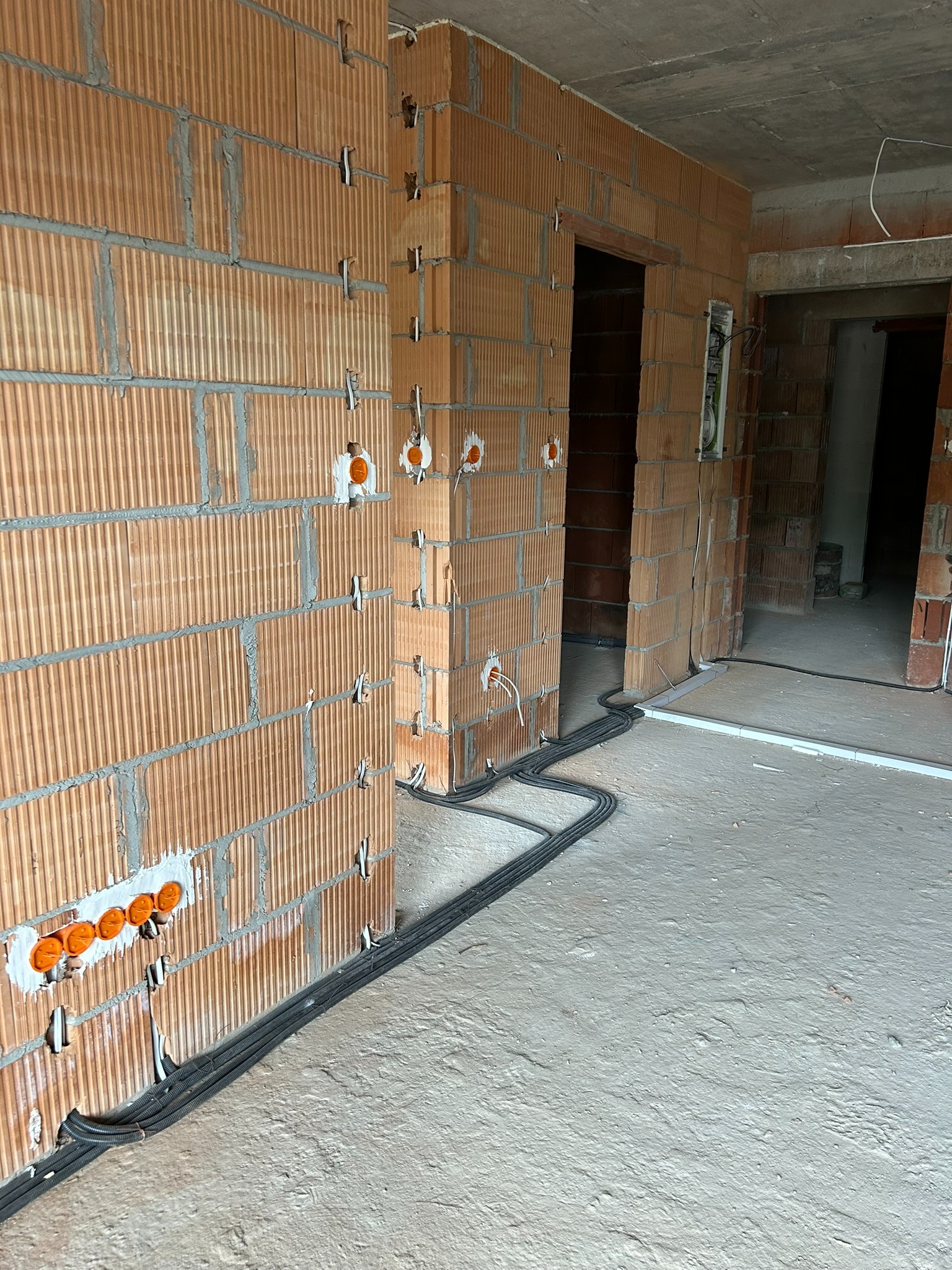 Instalacja elektryczna w trakcie wykonywania w Bytomiu: widoczne przewody ułożone na podłodze i puszki podtynkowe w ścianie z cegły kratówki.