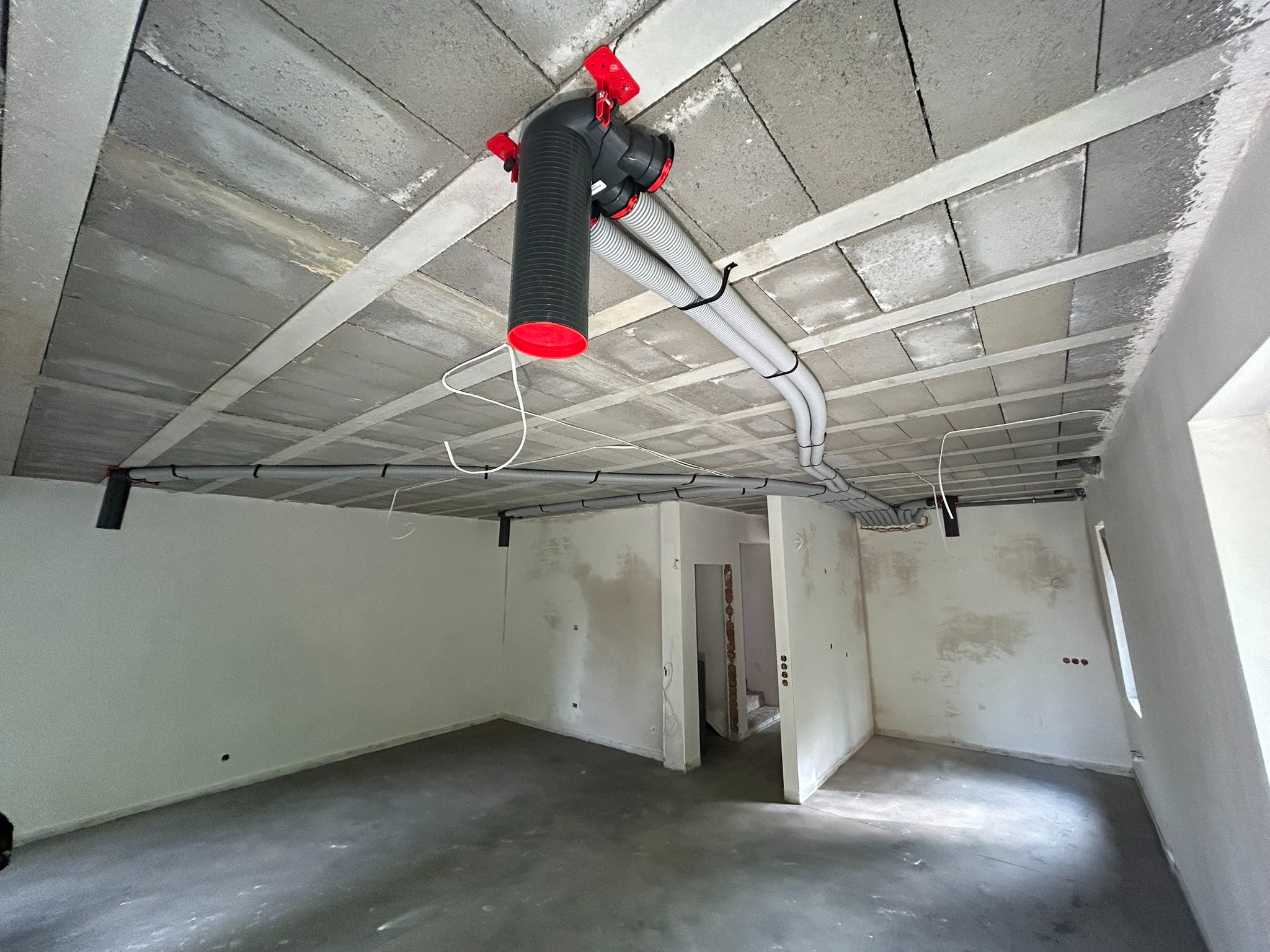 Szara instalacja wentylacyjna z czerwonymi elementami zamocowana do sufitu w surowym stanie w nowym pomieszczeniu.