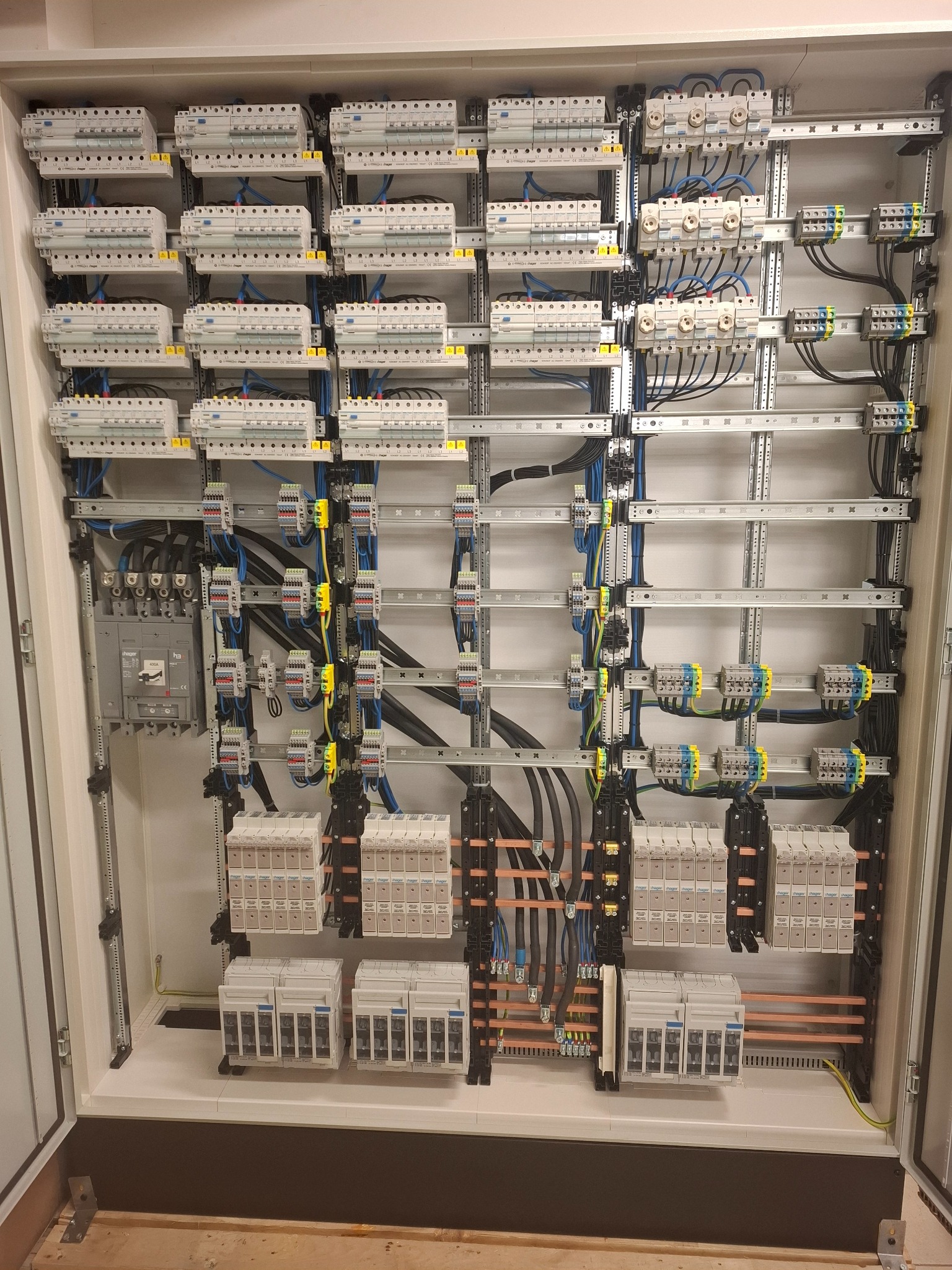 Rozbudowana szafa elektryczna z licznymi zabezpieczeniami, przewodami i szynami, widok z bliska na skomplikowaną instalację wewnątrz obudowy.