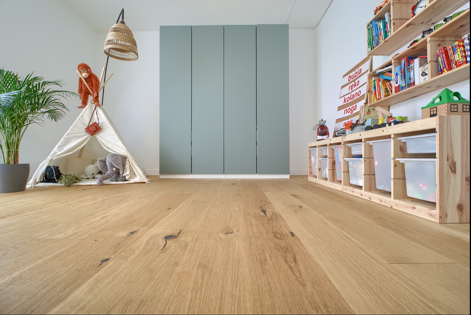 Jasna, dębowa posadzka w pokoju dziecięcym z tipi, regałem na zabawki i zieloną szafą w tle. Naturalne światło podkreśla strukturę drewna i przytulny charakter wnętrza.