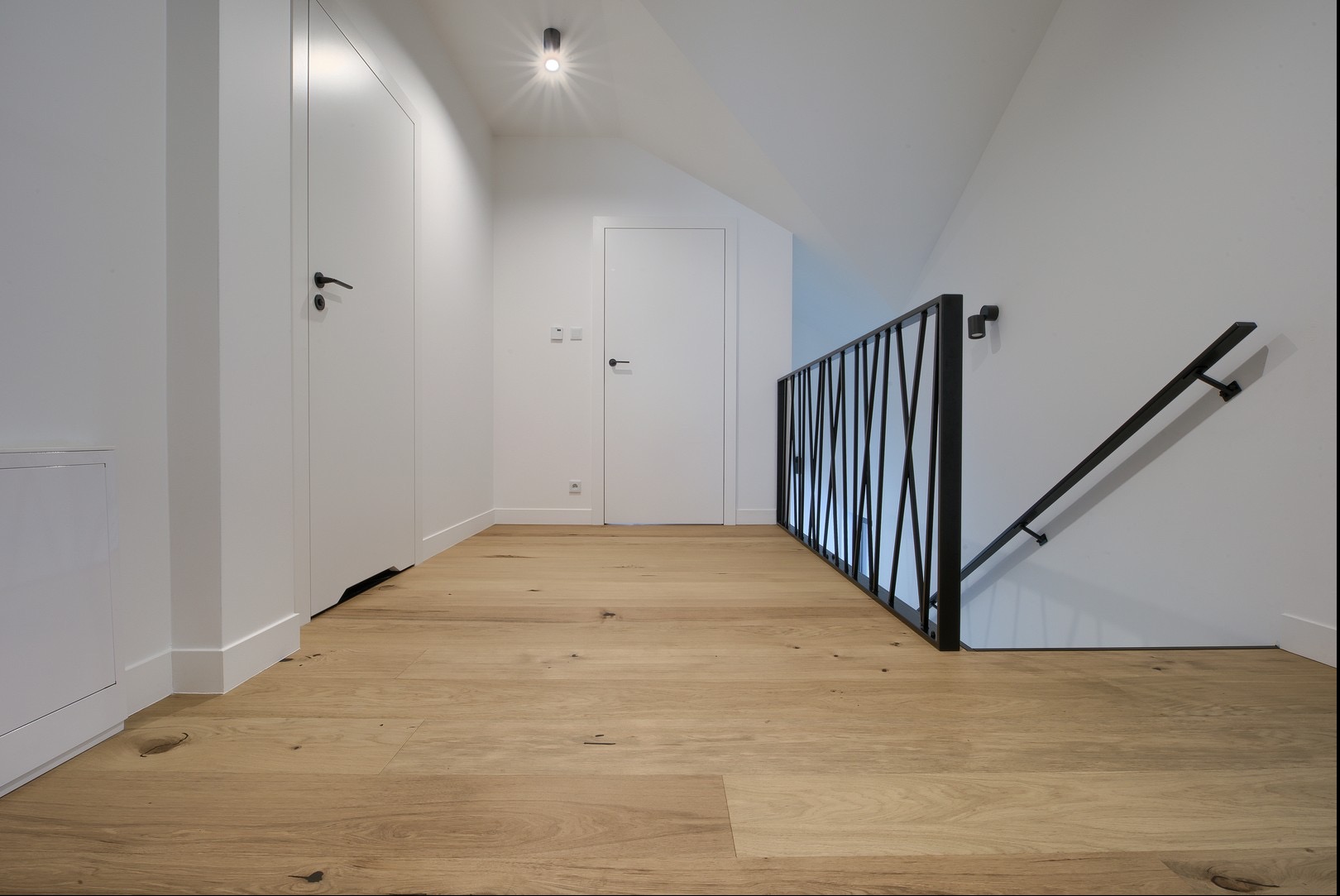 Jasne deski podłogowe w korytarzu z białą zabudową i czarną balustradą schodową w Suchej Beskidzkiej. Nowoczesne wykończenie wnętrza, naturalne drewno.