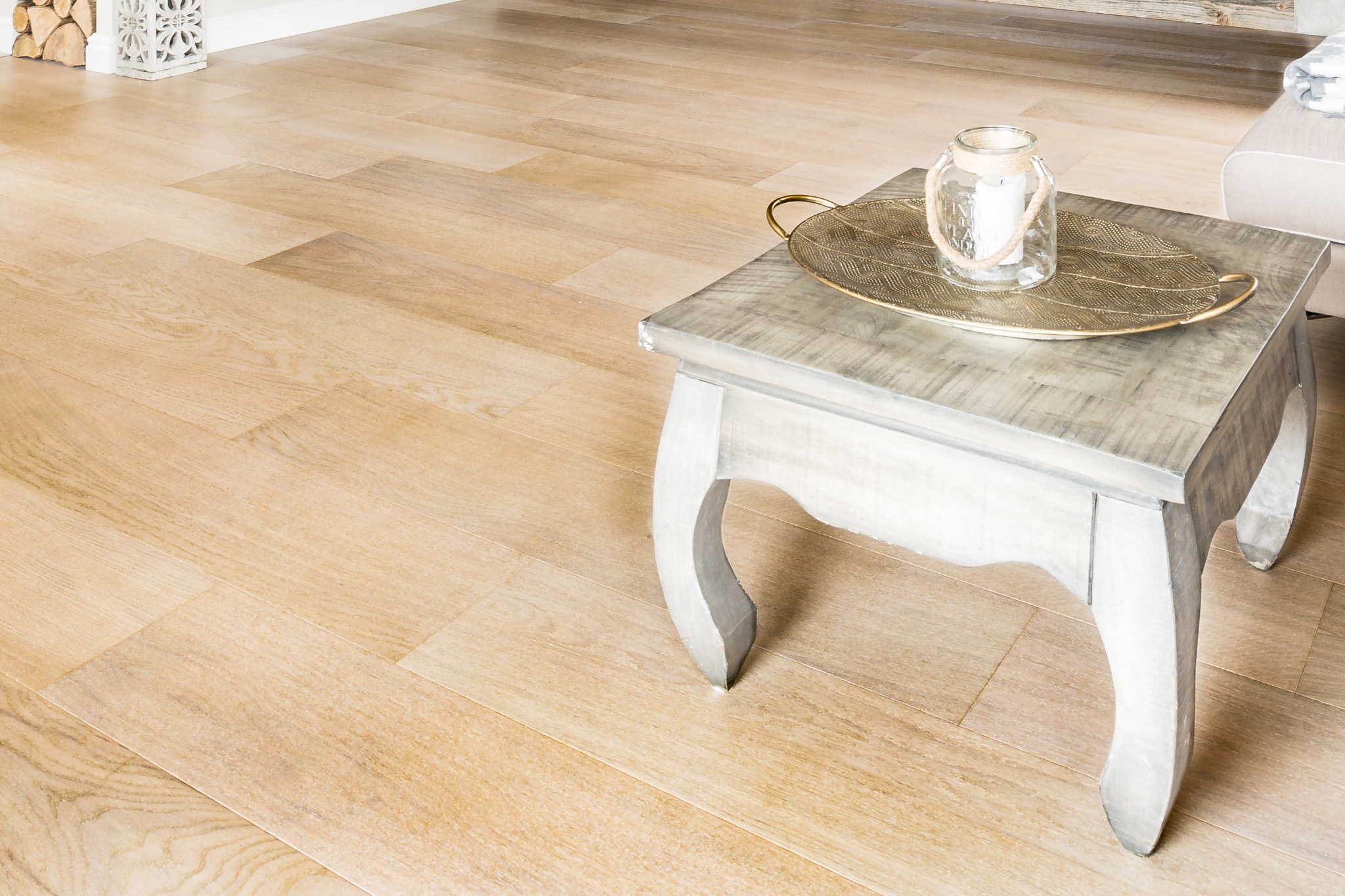 Jasne panele podłogowe ułożone w deseni cegiełki, z widocznym stolikiem kawowym i dekoracją. Naturalne światło podkreśla strukturę drewna.