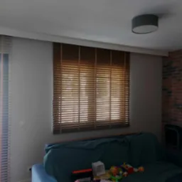 Brązowe poziome lamele okienne zamontowane w salonie z ceglaną ścianą, widoczne zabawki na sofie.