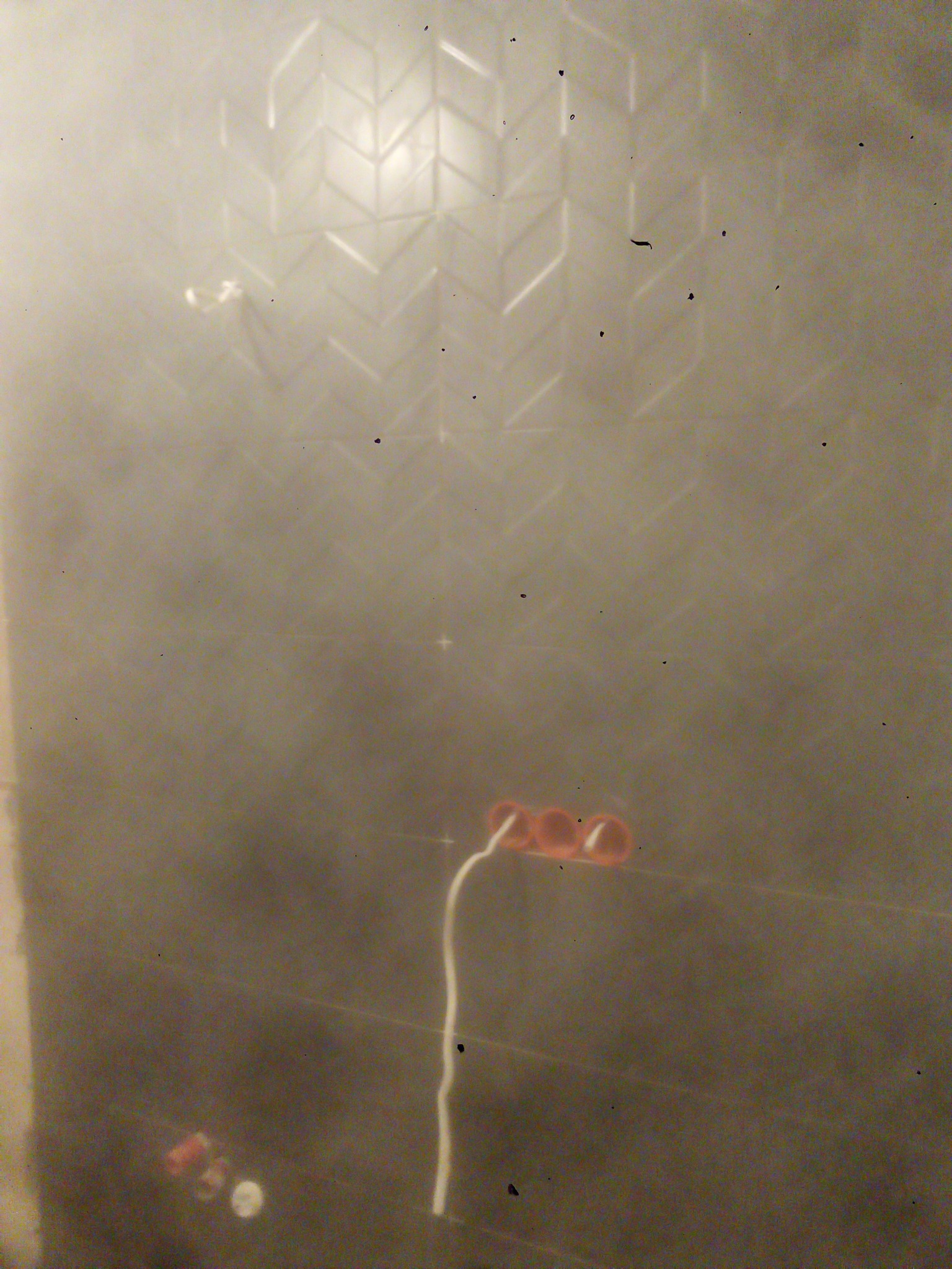 Ściana w trakcie układania płytek w jodełkę w łazience w Warszawie, widoczne puszki elektryczne i wystający kabel.