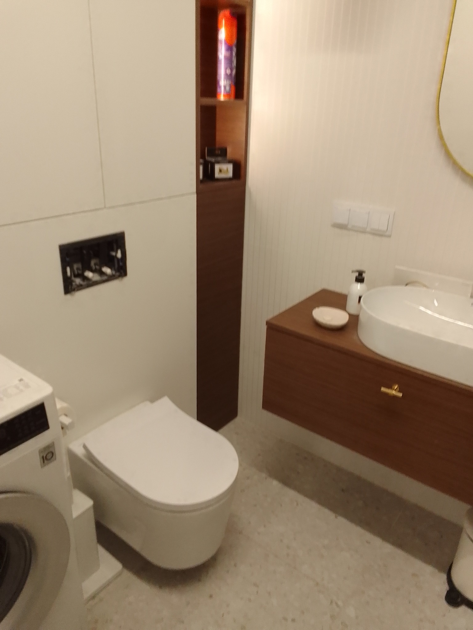 Nowoczesna łazienka z wiszącą toaletą, umywalką nablatową na drewnianej szafce, pralką LG oraz wysoką brązową szafką z półkami.