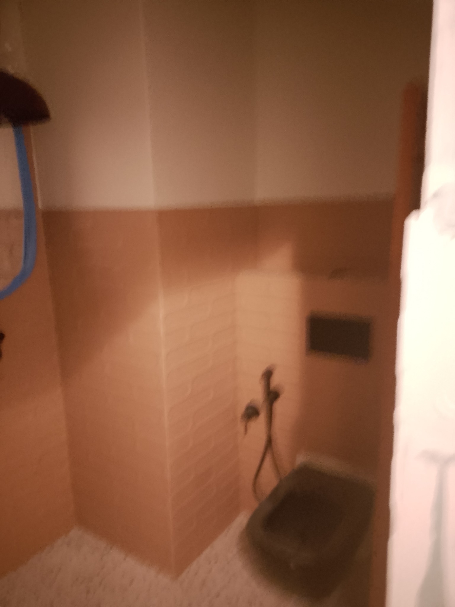 Ukończona łazienka z bidetem i brązowymi płytkami na ścianach do połowy wysokości. Kabina prysznicowa z niebieskim elementem. Widok z perspektywy wejścia.