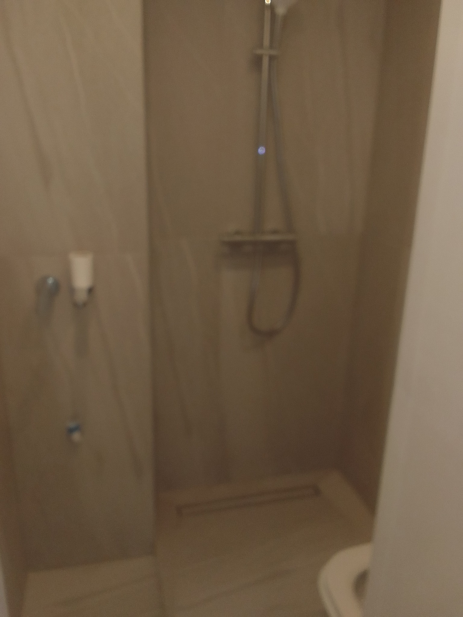 Minimalistyczna kabina prysznicowa z beżowymi płytkami imitującymi marmur i prostą armaturą. Widoczny odpływ liniowy.