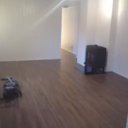 Pokój po ułożeniu paneli podłogowych, widoczny odkurzacz i piec wolnostojący.