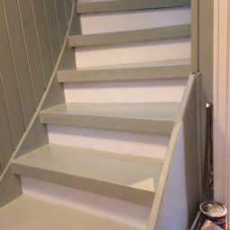 Prywatny wykonawca - Schody spiralne pomalowane na jasny, pastelowy odcień zieleni, z widoczną puszką farby i resztkami materiałów po malowaniu u dołu schodów.