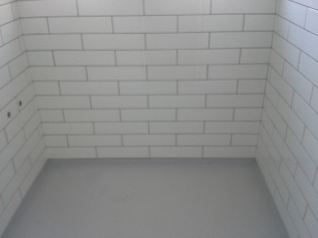 Wnętrze wykończonej łazienki z białymi, prostokątnymi płytkami na ścianach i szarą posadzką.