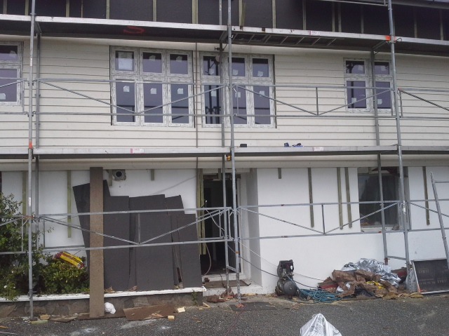 Dom w trakcie prac elewacyjnych, widoczne rusztowania, ocieplenie, fragmenty elewacji oraz narzędzia.