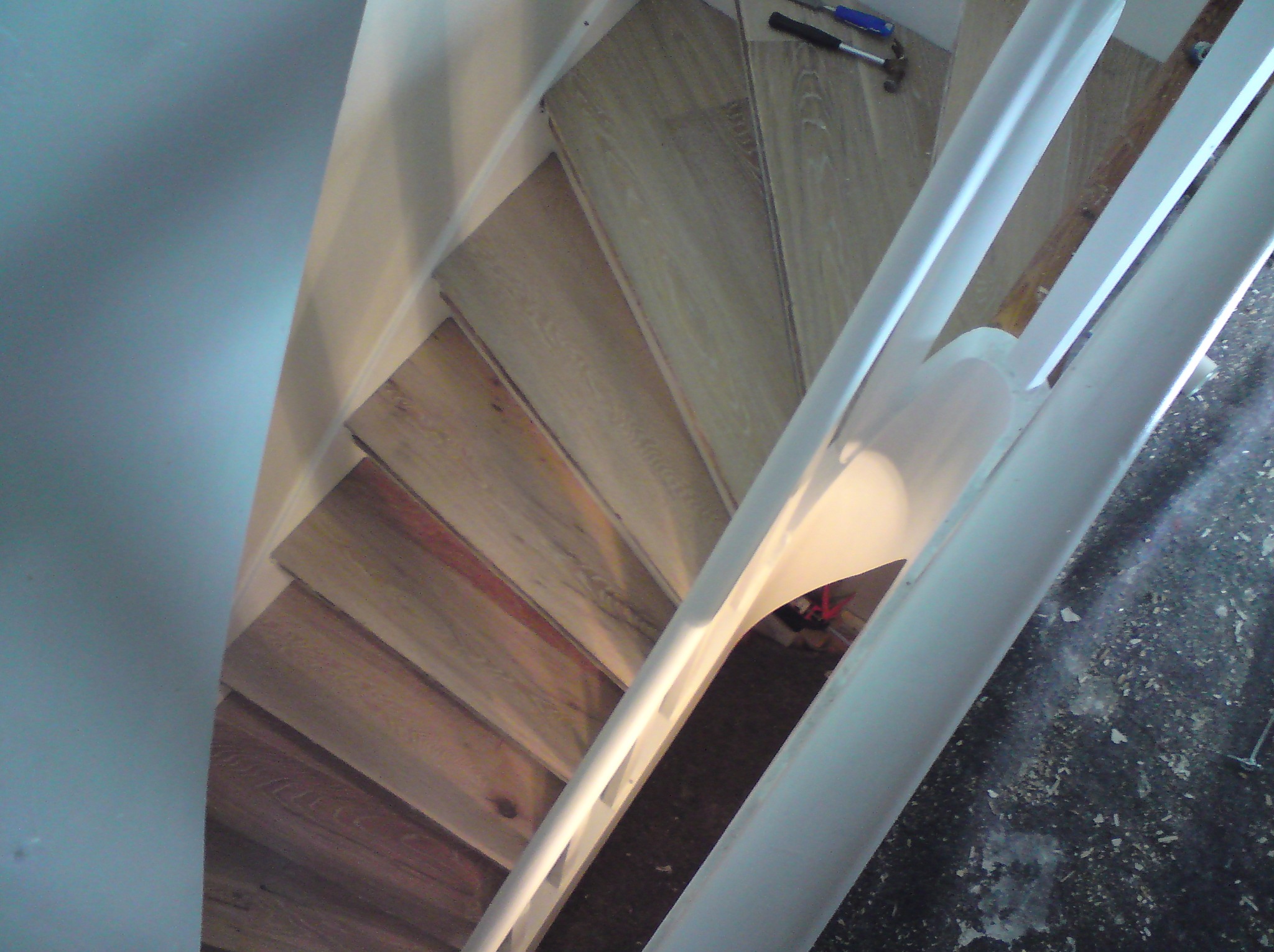 Ukończone schody z drewnianymi panelami, widok z góry, biała balustrada, młotek leżący na jednym ze stopni.