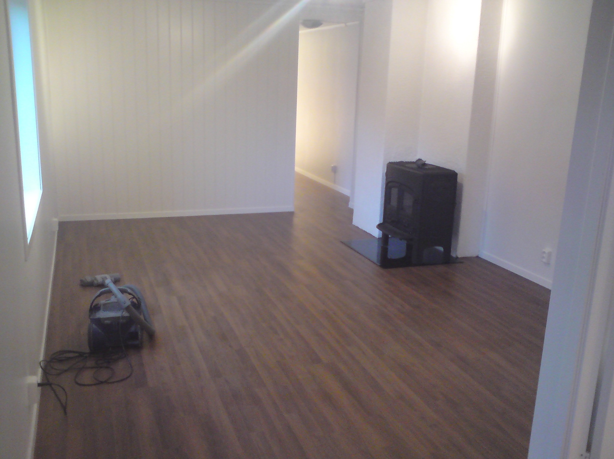 Pokój po ułożeniu paneli podłogowych, widoczny odkurzacz i piec wolnostojący.