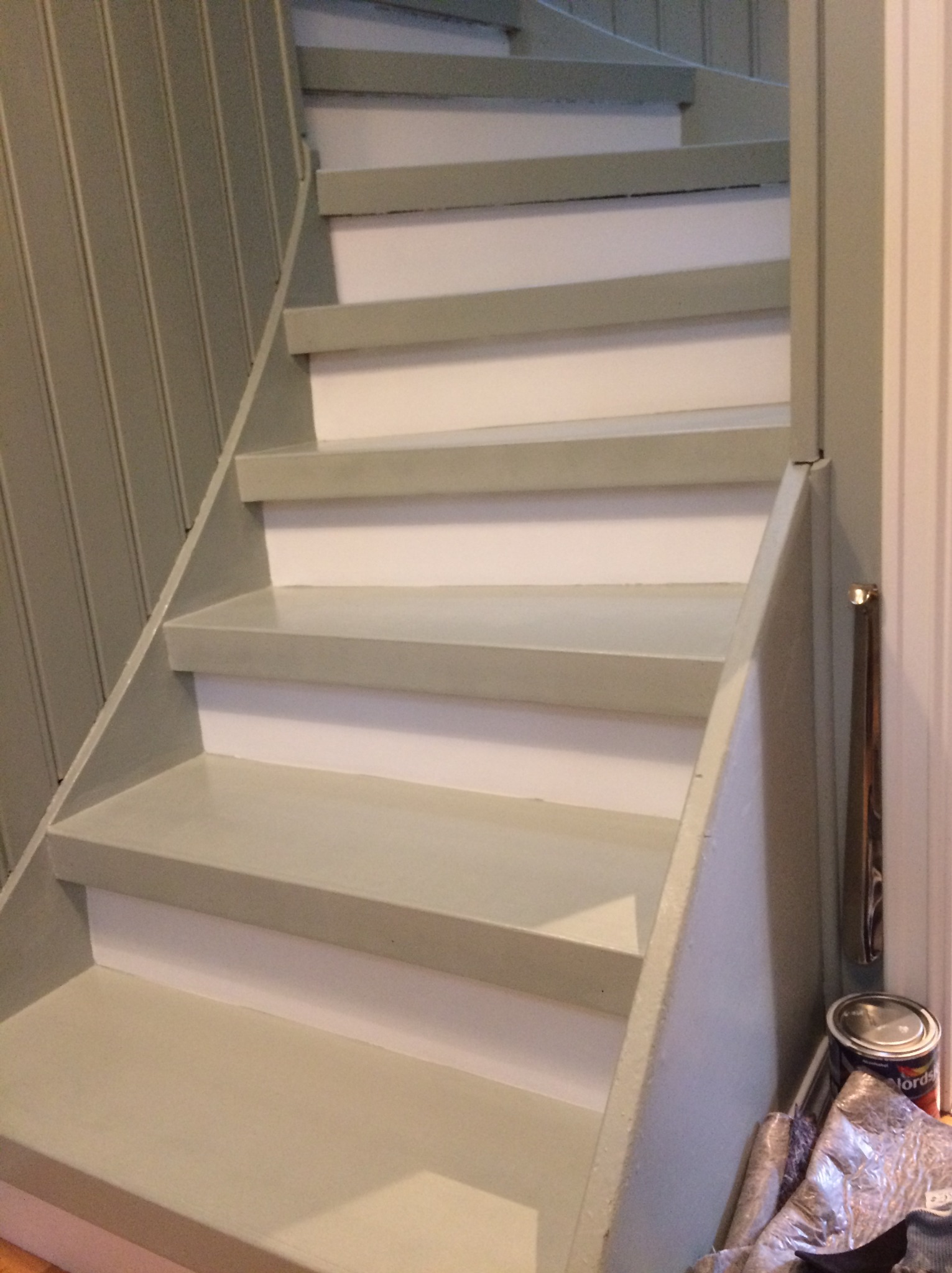 Schody spiralne pomalowane na jasny, pastelowy odcień zieleni, z widoczną puszką farby i resztkami materiałów po malowaniu u dołu schodów.