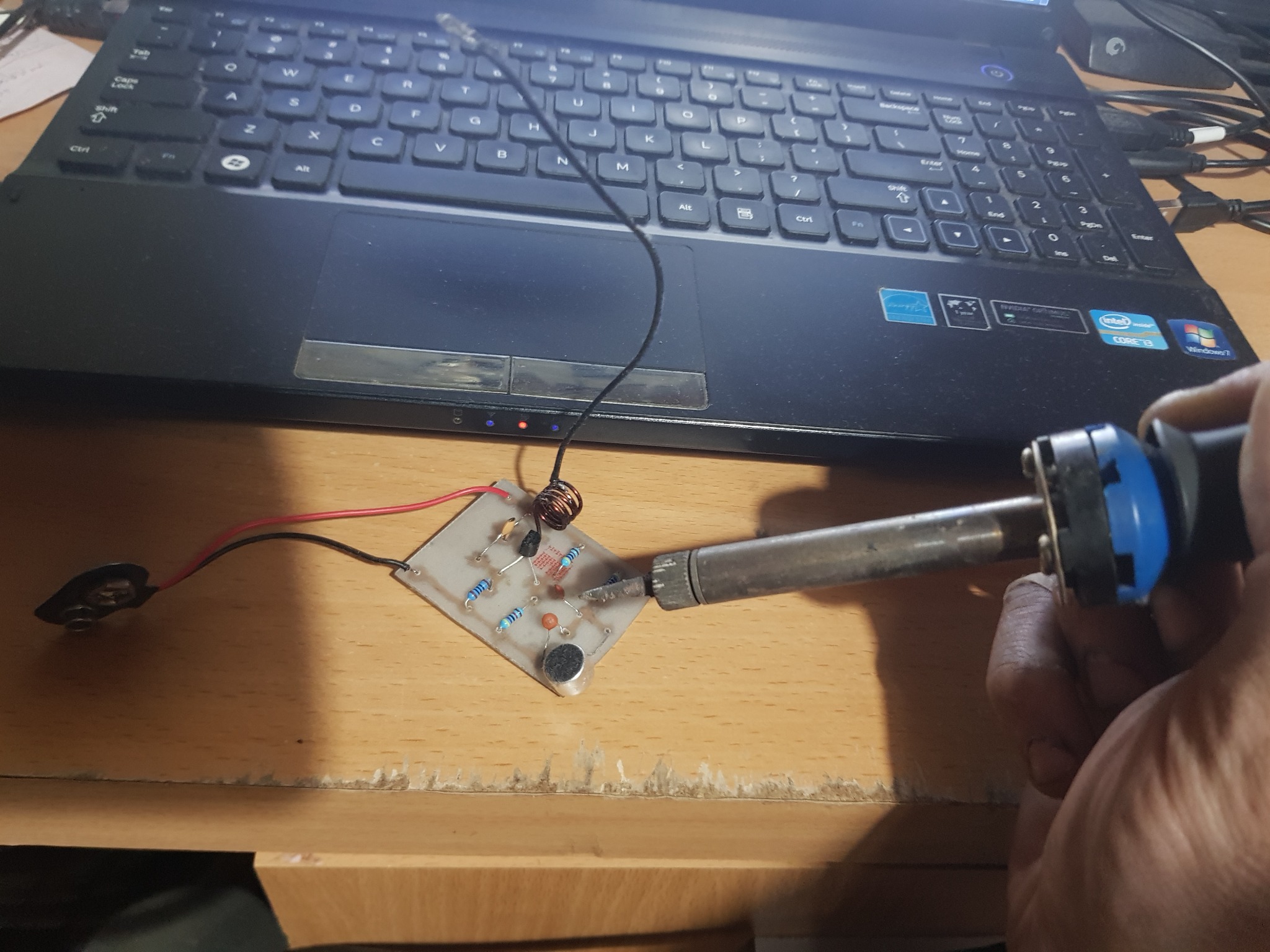 Lutowanie elementów elektronicznych na płytce drukowanej, widoczny laptop w tle, zasilanie z baterii 9V.