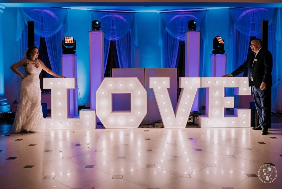 Para młoda pozuje obok podświetlanego napisu LOVE na sali weselnej z niebieskim oświetleniem.