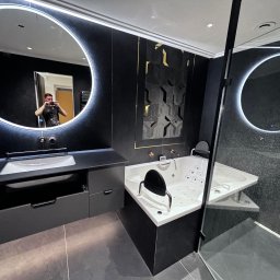 Gatkowski Łukasz - Nowoczesna łazienka w ciemnej kolorystyce z podświetlanymi lustrami, narożną wanną z hydromasażem i kabiną prysznicową ze szklanymi drzwiami, widoczne odbicie osoby robiącej zdjęcie w lustrze...