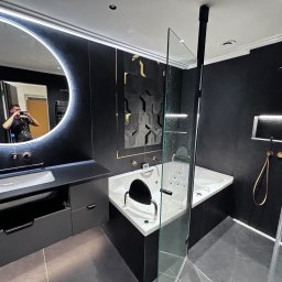 Gatkowski Łukasz - Nowoczesna łazienka z czarnymi ścianami, okrągłym podświetlanym lustrem odbijającym fotografa, białą wanną z hydromasażem i szklaną kabiną prysznicową.