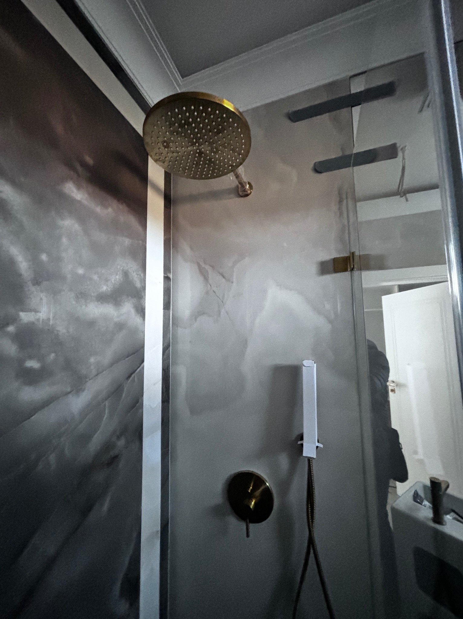 Nowoczesna kabina prysznicowa z deszczownicą w kolorze złotym, ściany wykończone szarą imitacją marmuru, widoczny panel sterujący i słuchawka prysznicowa.