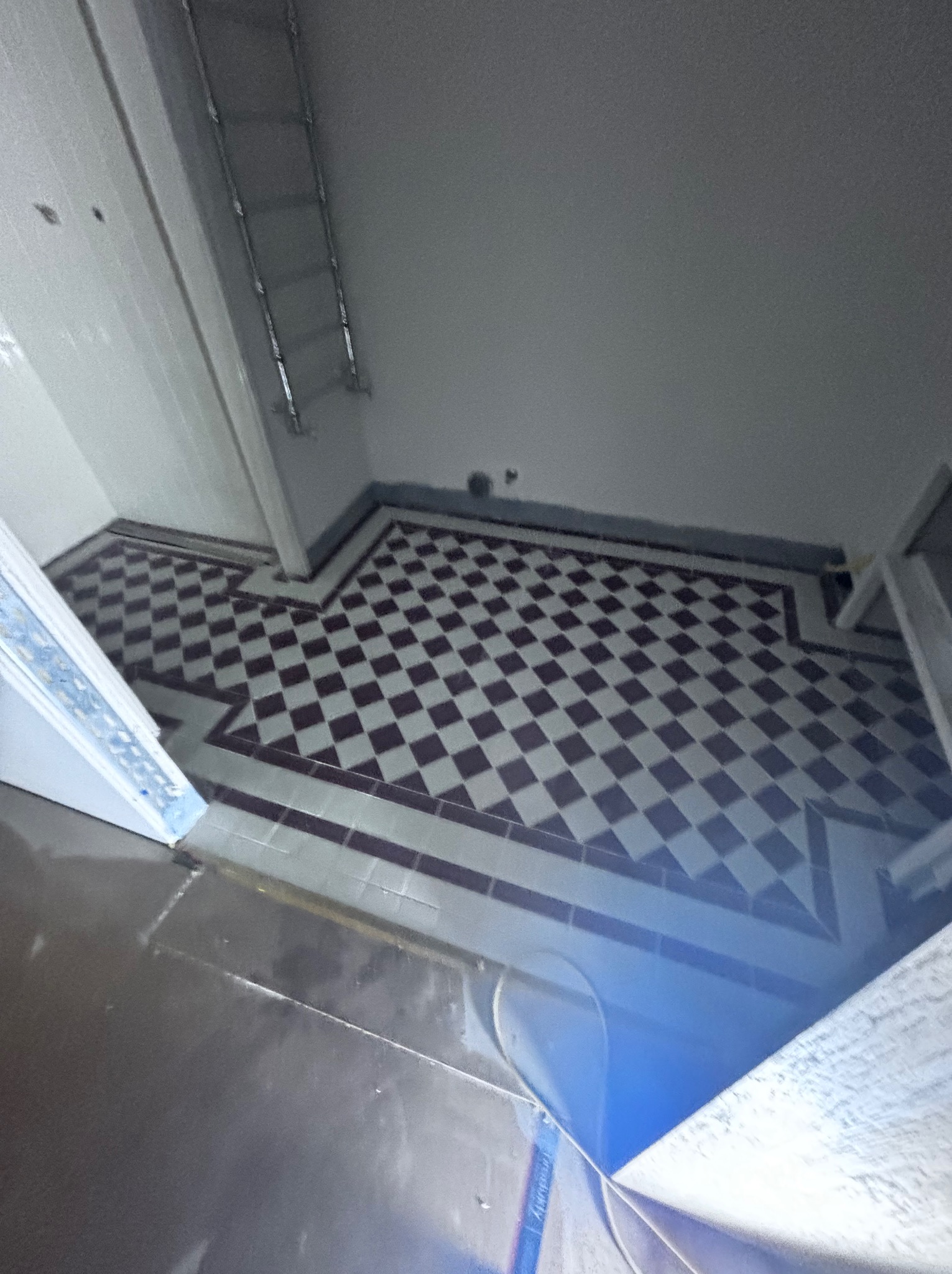 Ukończona podłoga w łazience z wzorem szachownicy, biało-czarne płytki ułożone w karo, widok z góry, częściowo widoczne ściany w kolorze białym.