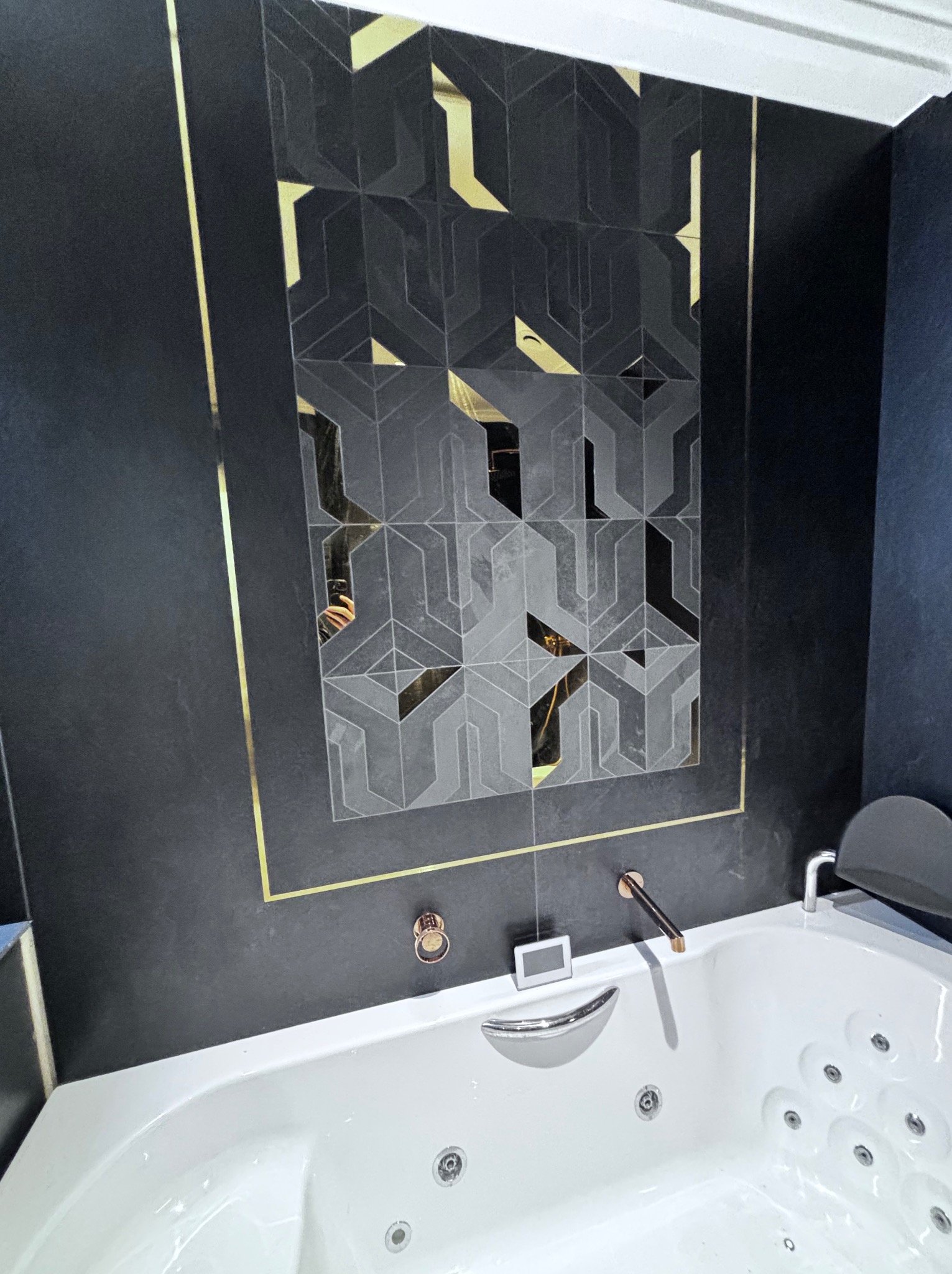 Nowoczesna łazienka z czarnymi ścianami, geometrycznymi płytkami z akcentami złota i białą wanną z hydromasażem.