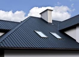 Nowoczesny, grafitowy dach z blachy trapezowej z dwoma oknami dachowymi, widoczny komin na tle błękitnego nieba z chmurami.