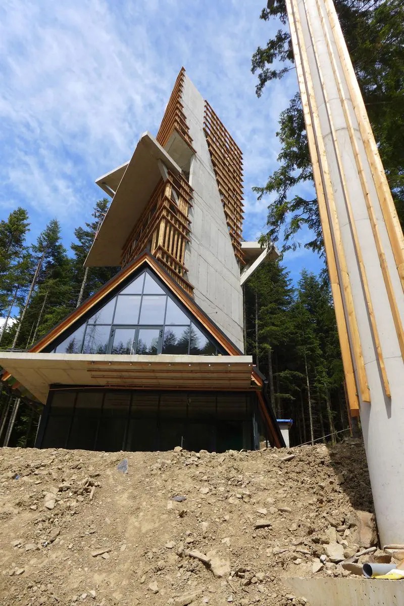 Nowoczesna wieża widokowa z betonu i drewna w lesie, widok z dołu na konstrukcję w trakcie budowy z widoczną ziemią i elementami szalunku.