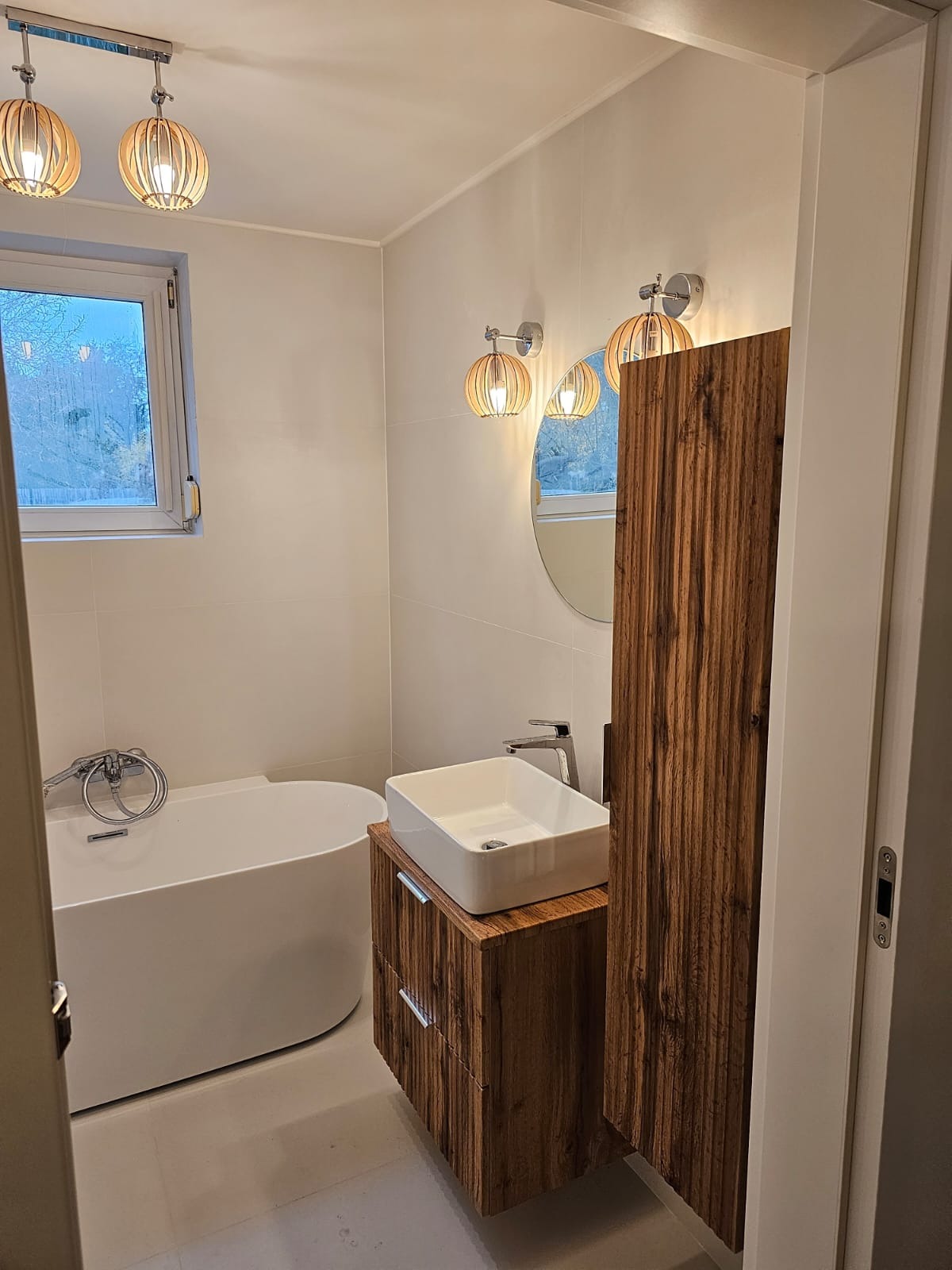 Nowoczesna łazienka z wolnostojącą wanną, umywalką nablatową na szafce z drewna egzotycznego i okrągłym lustrem podświetlonym dekoracyjnymi lampami