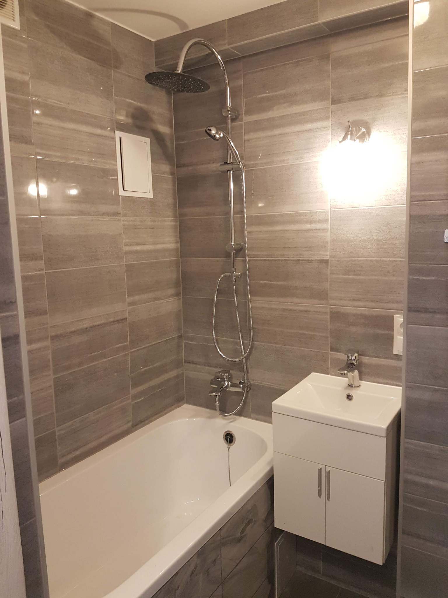 Nowoczesna łazienka z wanną, umywalką z szafką i szarą, poziomą glazurą imitującą kamień, oświetlona punktowym światłem.