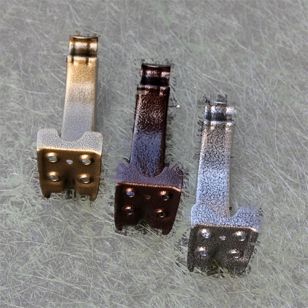 Trzy metalowe uchwyty rynnowe w różnych kolorach (złoty, brązowy, srebrny) prezentowane na teksturowanym tle, widoczne otwory montażowe.