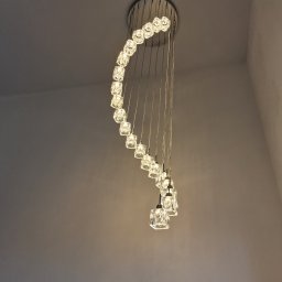 Energo-Instal Elektryk Śląsk - Spiralna lampa wisząca z kryształowymi elementami, zamontowana na suficie, oświetlona ciepłym światłem, widok od dołu.