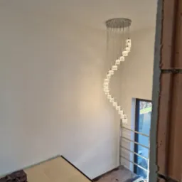 Spiralny żyrandol z kryształkami, widoczny z dołu, zamontowany w nowym domu w trakcie wykańczania, z rusztowaniem i zabezpieczeniem podłogi.