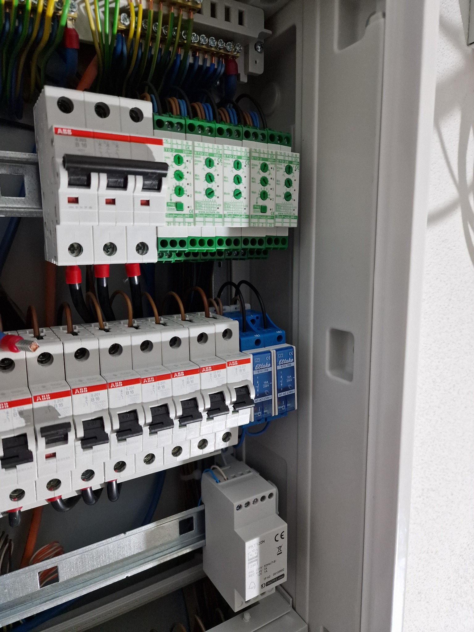 Wewnętrzny widok rozdzielnicy elektrycznej z zainstalowanymi bezpiecznikami ABB, modułami Eltako i przewodami w kolorowej izolacji, zamontowanymi na szynie DIN.