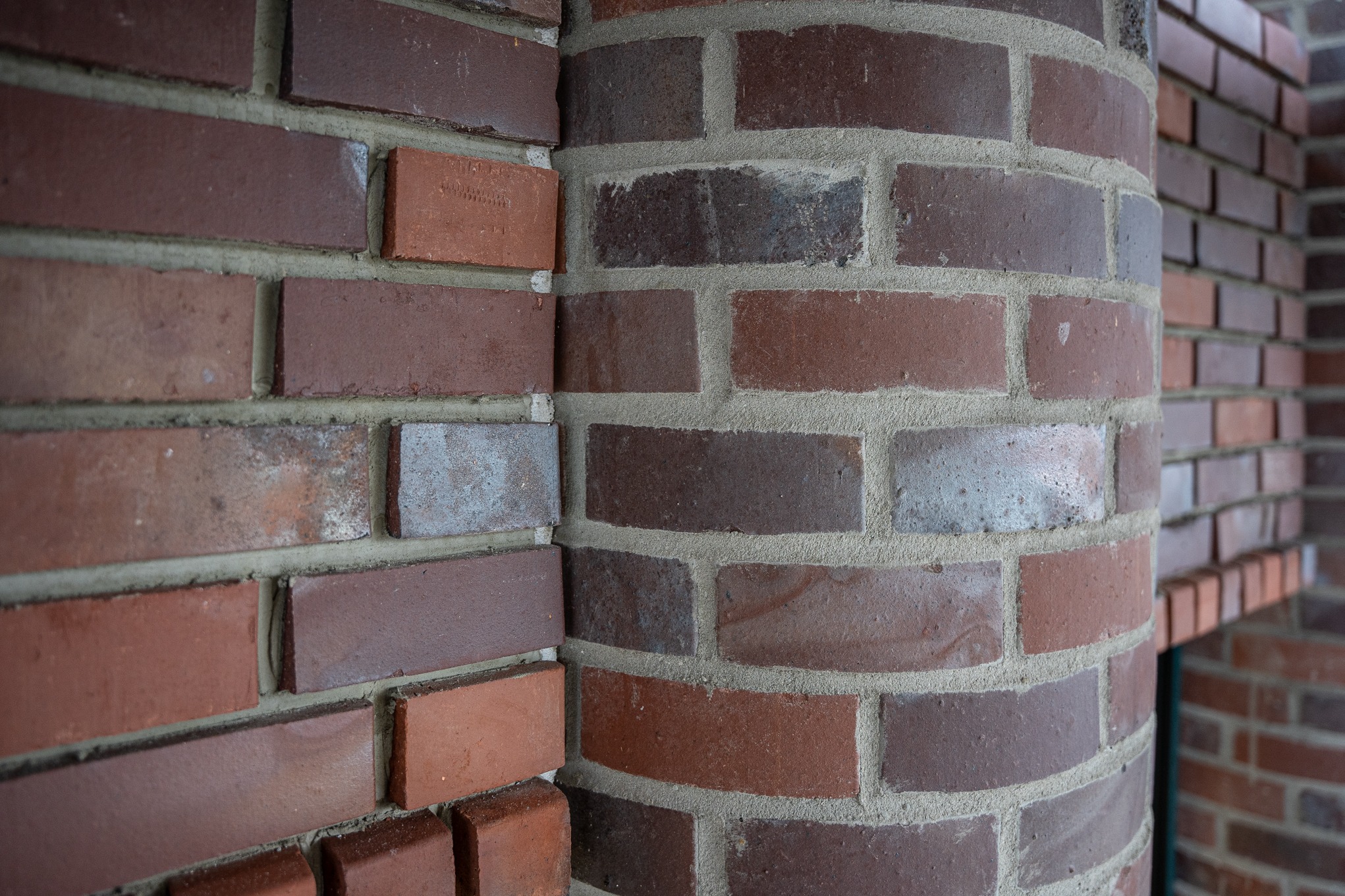 Fragment elewacji z czerwonej cegły z zaokrąglonym narożnikiem, widoczne spoiny i faktura cegieł.