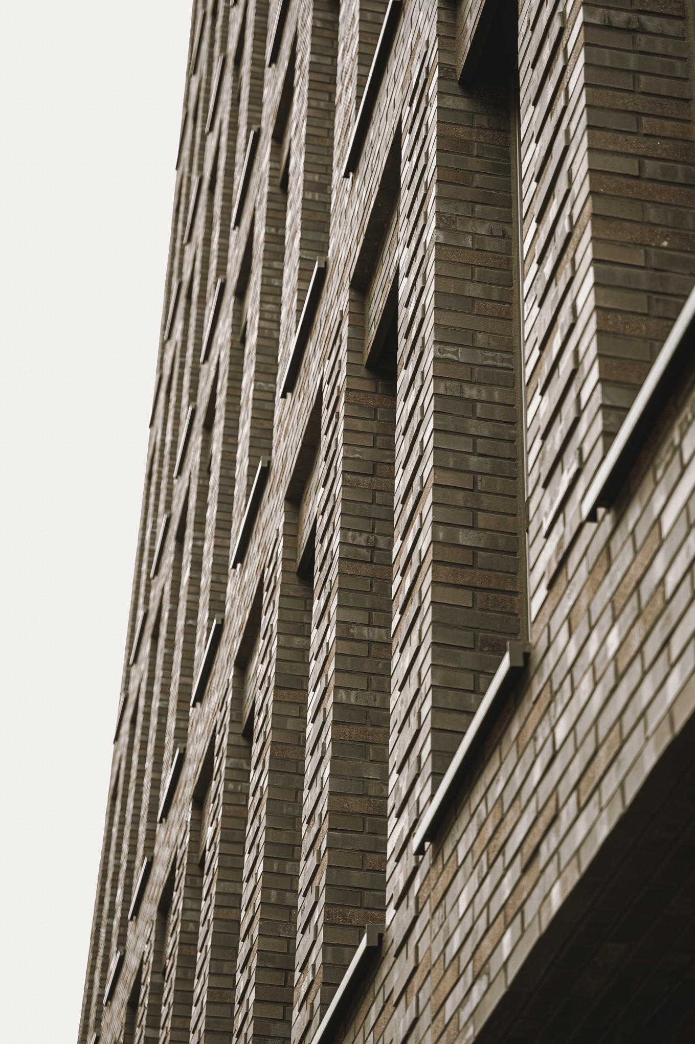 Wysoki budynek z ceglaną elewacją, widok z dołu ukazujący regularny układ okien i fakturę cegieł w stonowanej kolorystyce.