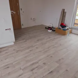 Jasne panele podłogowe w nowym wnętrzu w Świnoujściu, widoczne narzędzia i materiały wykończeniowe, surowy stan ścian i instalacje.