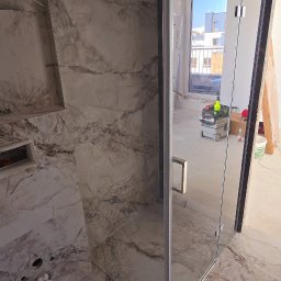 TŁ Andrii Smaliuk - Szklana kabina prysznicowa z marmurowymi płytkami w łazience. Widoczne narzędzia i materiały budowlane, co sugeruje trwający montaż.